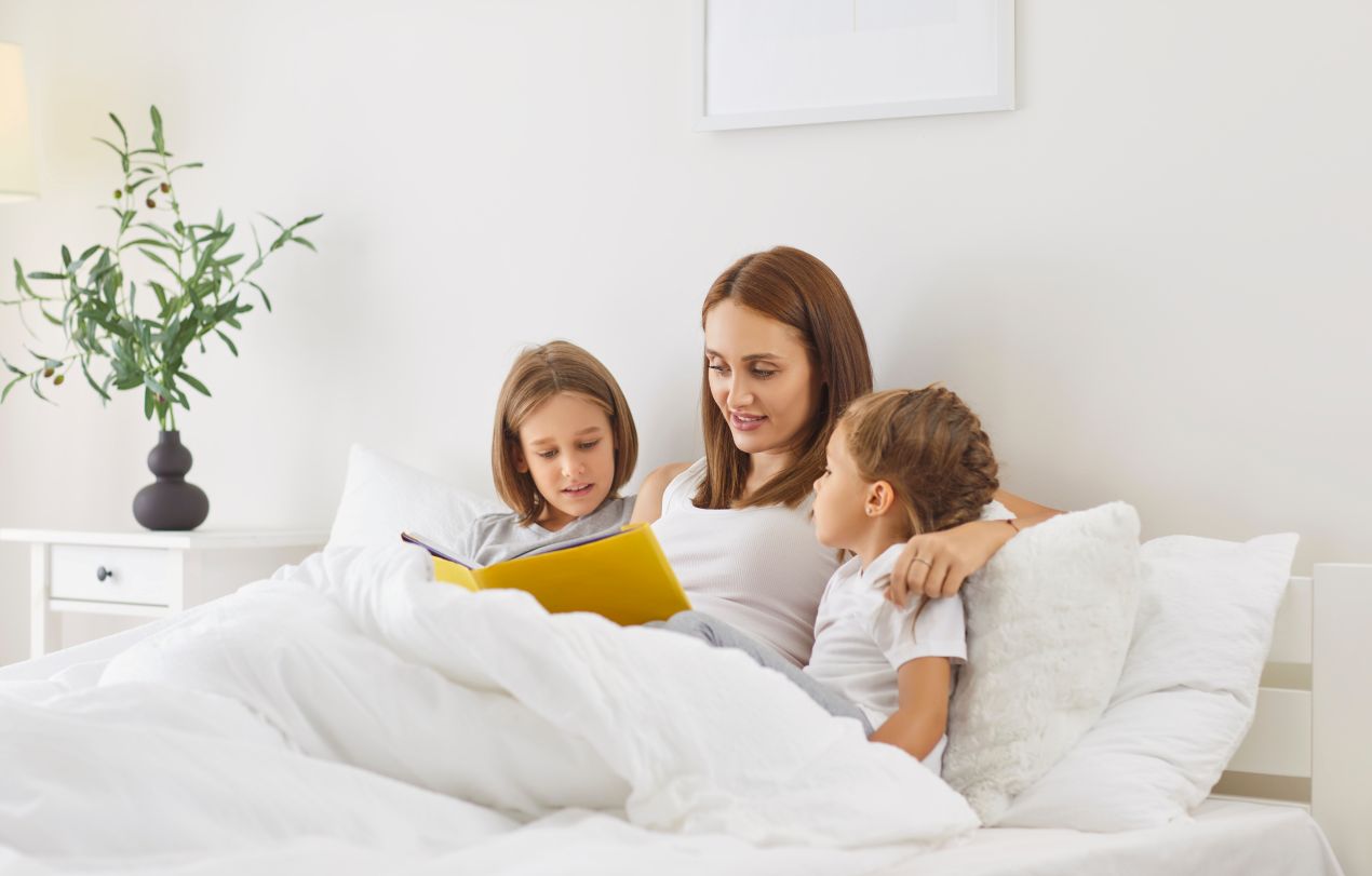 Mutter liest zwei Kindern auf dem Bett vor, alle liegen unter einer Alpaka Bettdecke