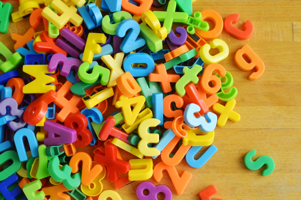 Bunte Magnetbuchstaben und Zahlen zur Sprachfoerderung bei Kindern in der Logopaedie Holzwickede auf einem Holztisch verteilt