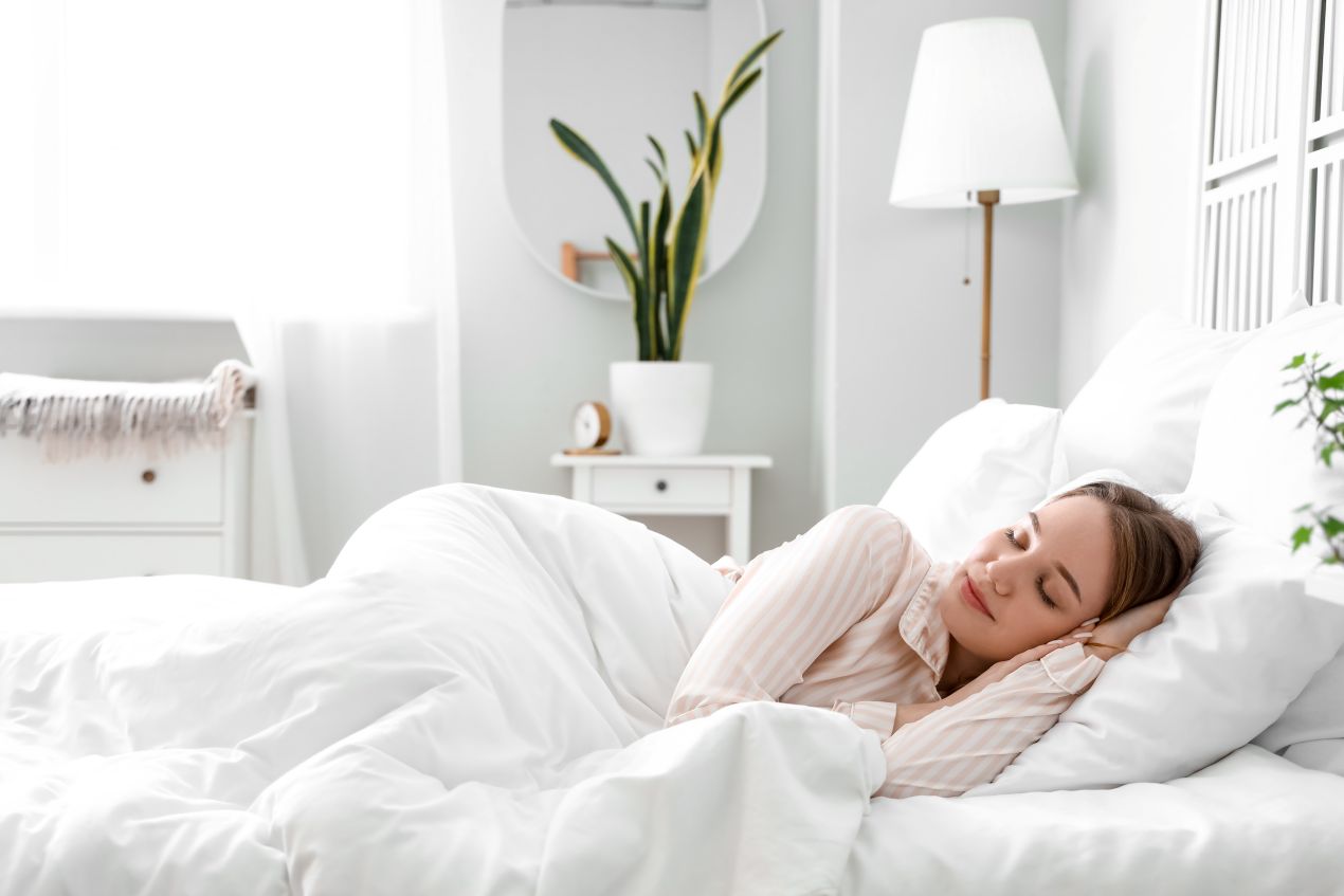 Junge Frau schlaeft unter einer Alpaka Bettdecke in einem hellen Schlafzimmer